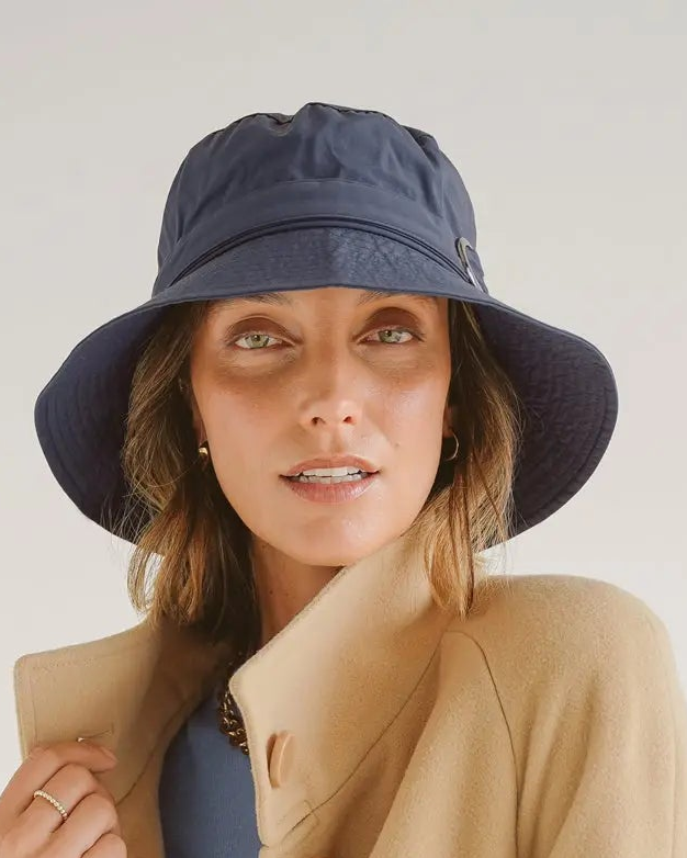 Woman wearing a beige coat and navy bucket hat on a plain background
